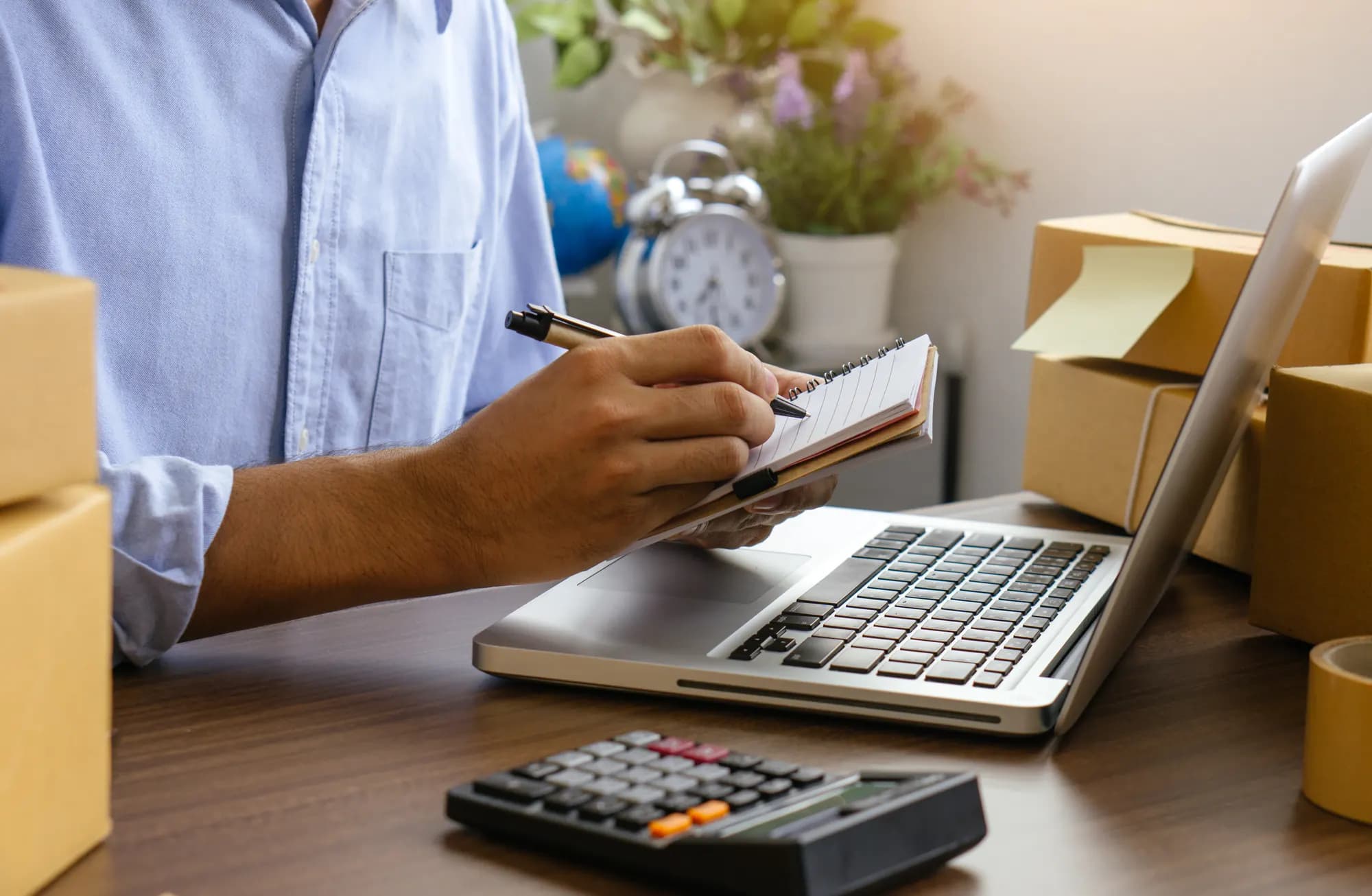 Gestor anotando preços ao lado do notebook e da calculadora